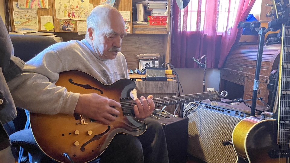François Lemieux dans son atelier de musique, tenant une guitare. 