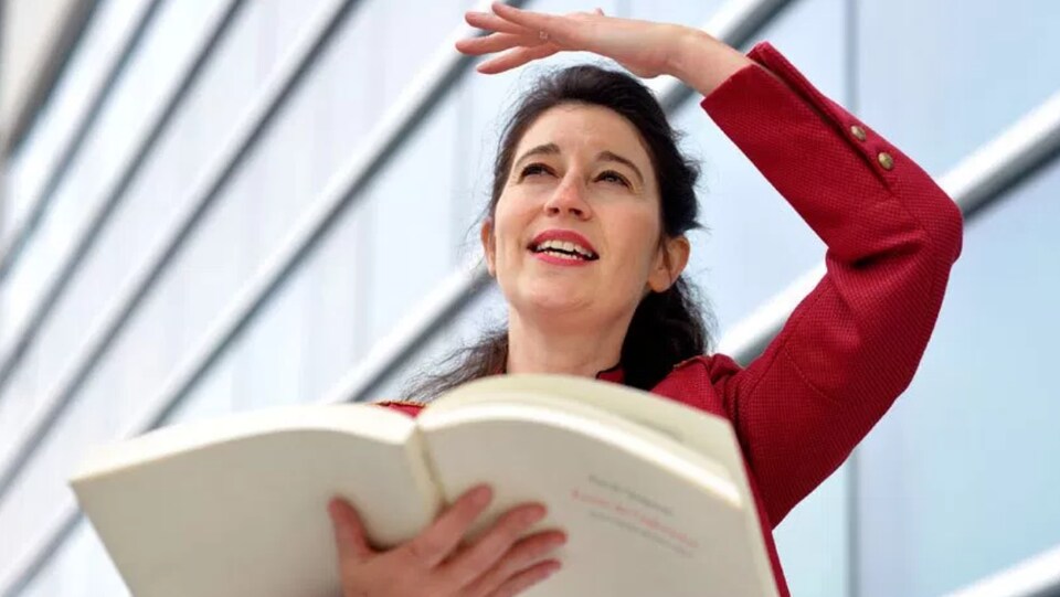 Une femme qui lit un livre en faisant un mouvement de bras.