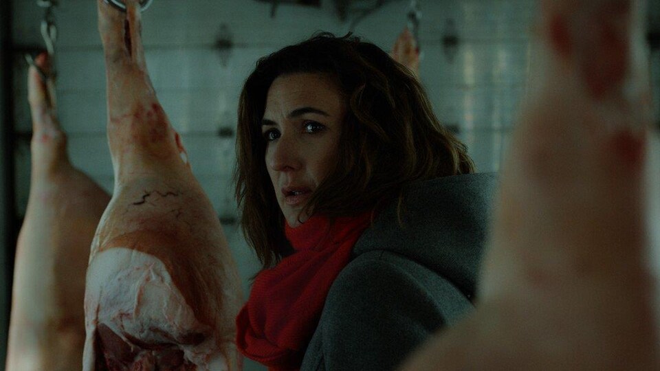 Une actrice jette un regard inquiet parmi des carcasses de porcs suspendues. 