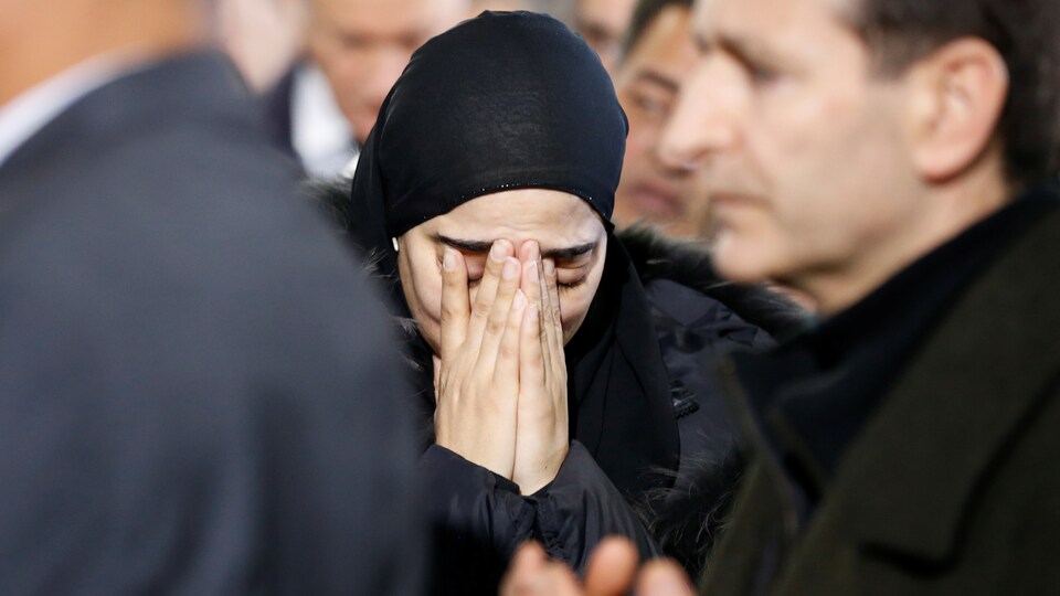 Une femme portant le voile qui semble triste et qui porte ses mains à son visage lors des funérailles de victimes de l'attentat de Québec.