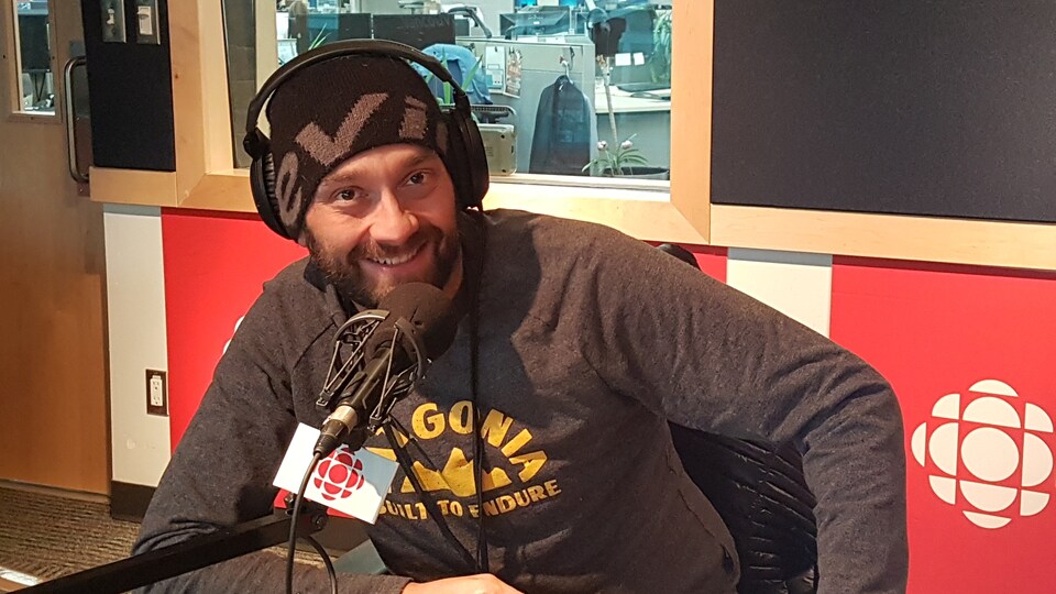 Un homme est assit devant un micro dans un studio de radio