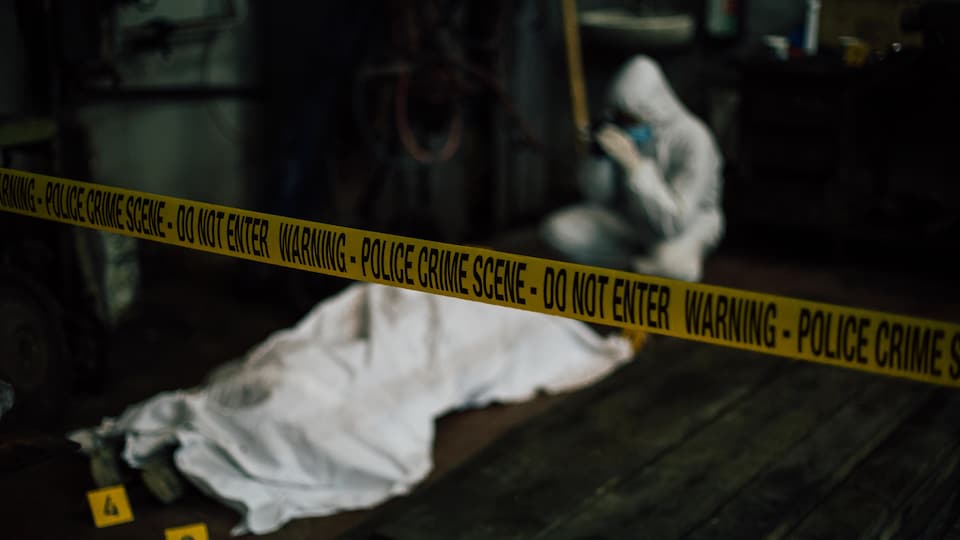 Une scène de crime avec un ruban jaune de la police. Sur le sol, un corps recouvert d'un drap. 