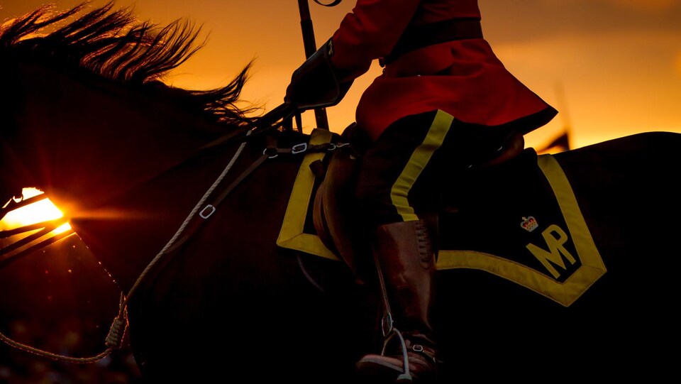 Un policier de la GRC à dos de cheval, avec le soleil se couchant en arrière-plan.