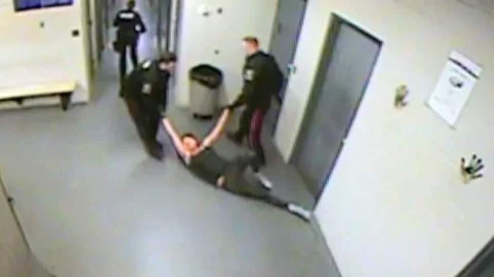 Deux agents traînent Genesta Garson par les bras sur un sol de ciment.