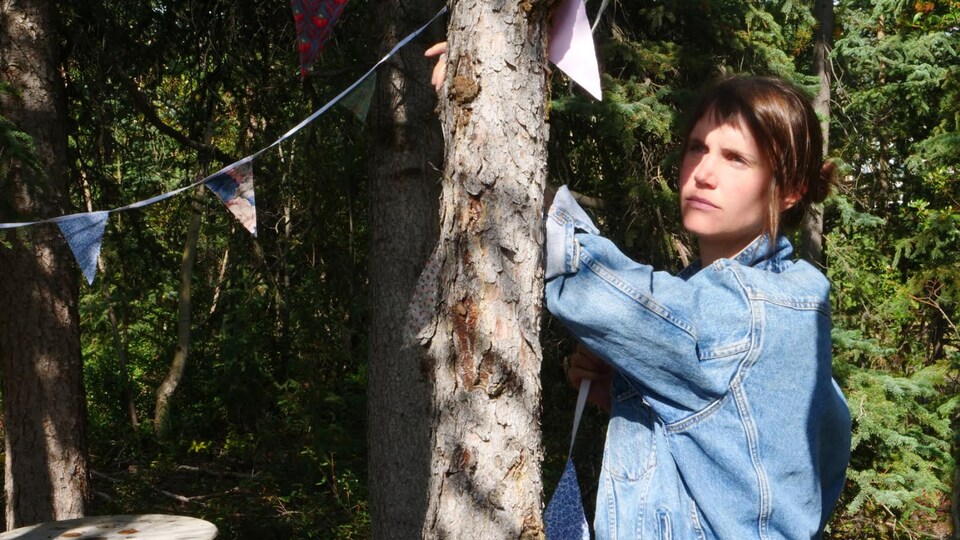 arbres, fanions et jeune femme en blouson Levi's bleu ciel dans une forêt boréale semi-éclairée