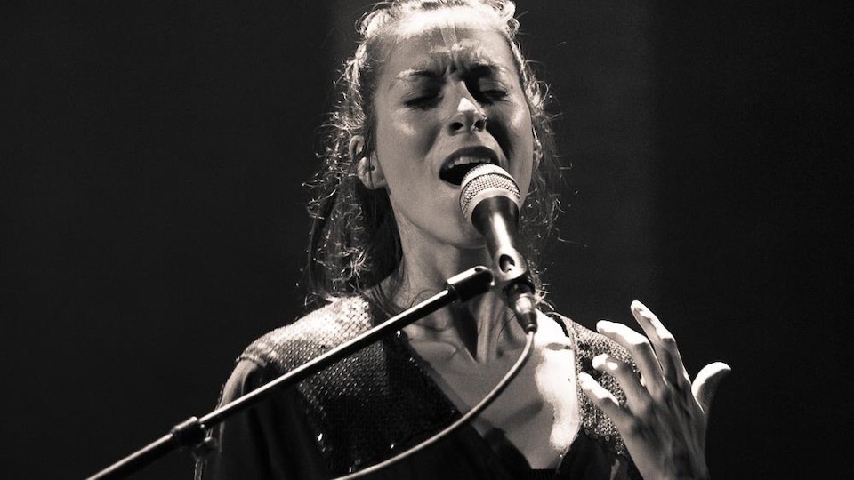Jeune dame aux longs cheveux, yeux fermés, chante dans un microphone.