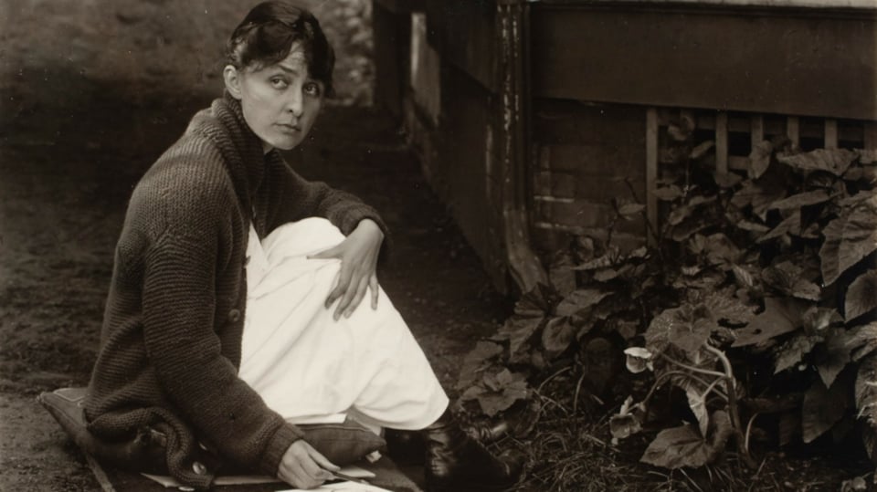 Photo de Georgia par Alfred Stieglitz, assise sur le sol avec boite de peinture.