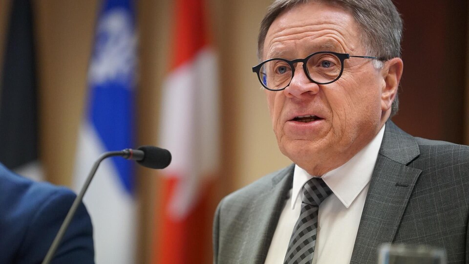 Le maire Gilles Lehouillier prend la parole devant les drapeaux du Québec et du Canada.