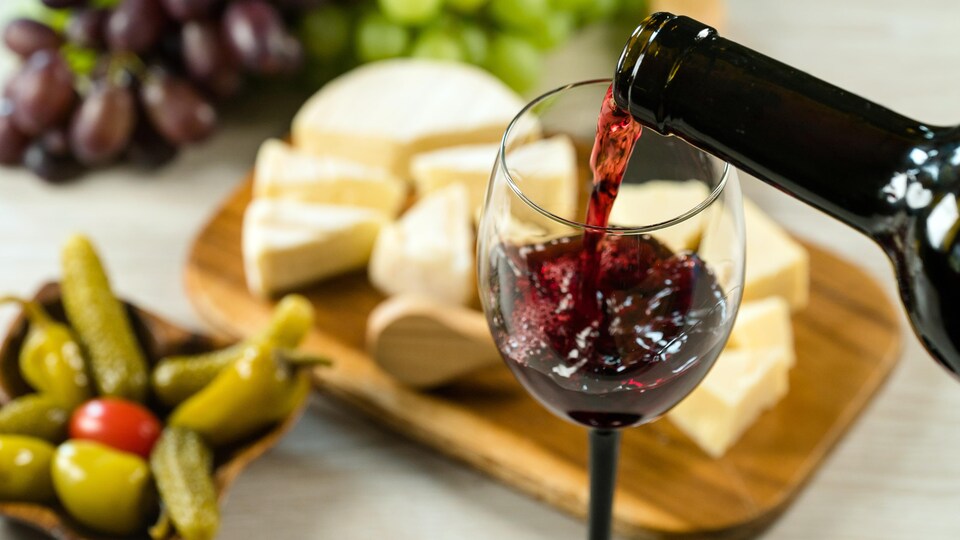 Du vin rouge est versé dans une coupe posée sur une table où sont disposés des hors-d'œuvre.