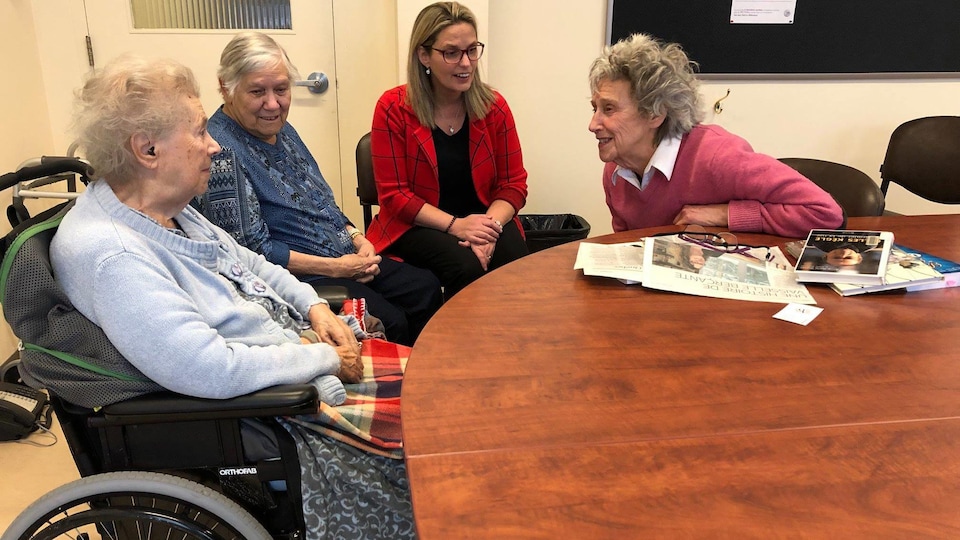 Quatre femmes, trois sont âgées, dont une en fauteuil roulant, discutent à table