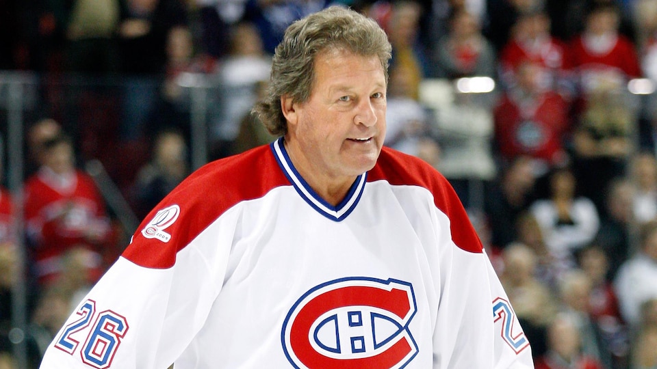 Pierre Bouchard porte un chandail des Canadiens de Montréal et un bâton de hockey sur la patinoire du Centre Bell.