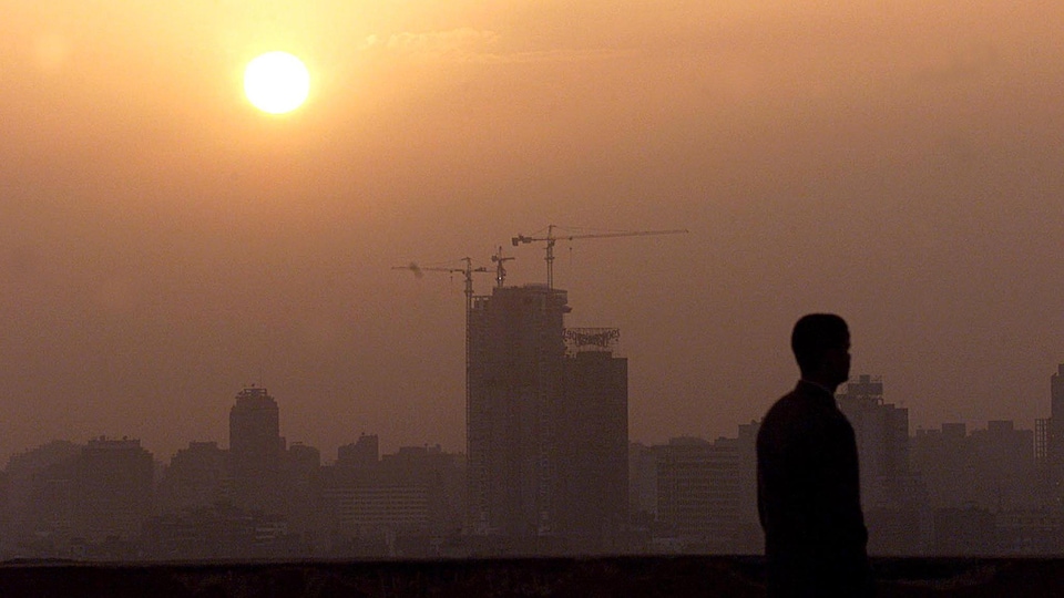 Le smog domine une ville au coucher du soleil. En contre-jour se trouve un homme en avant-plan.