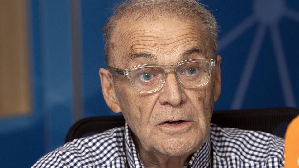 Un homme portant des lunettes parle devant un micro orange.