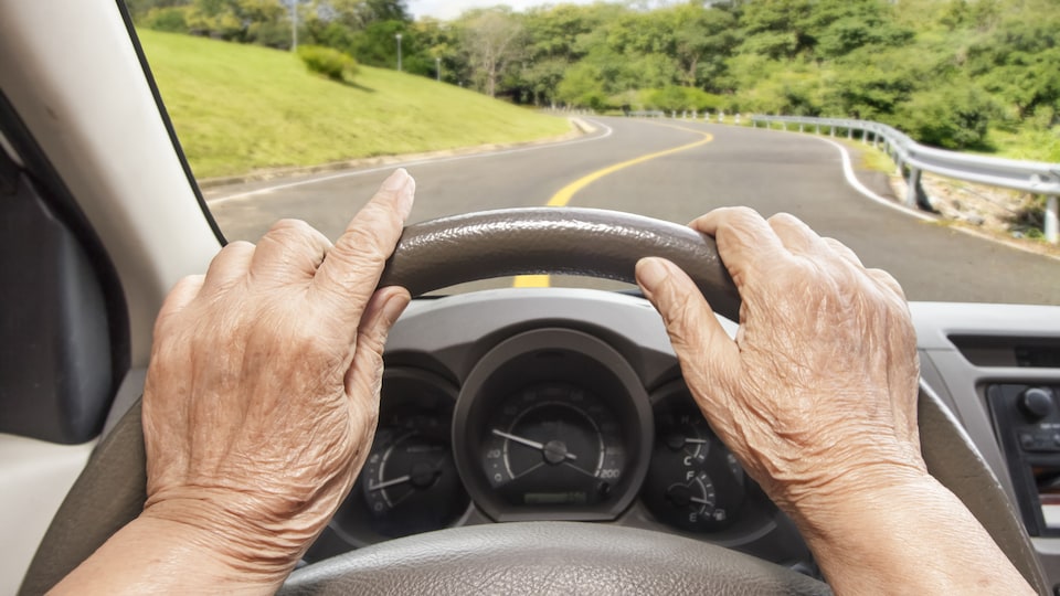 Une personne âgée circule en voiture sur une route.