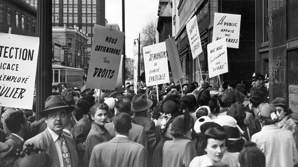 Photo en noir et blanc montrant un foule d'hommes et de femmes tenant des pancartes.