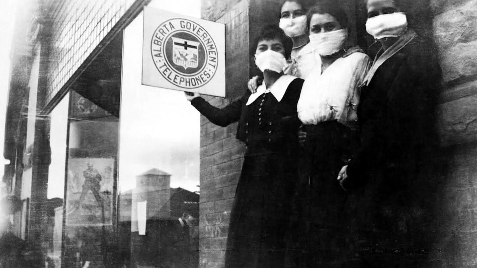 Quatre jeunes femmes portant des masques devant un édifice. Photo noir et blanc d'époque. 

