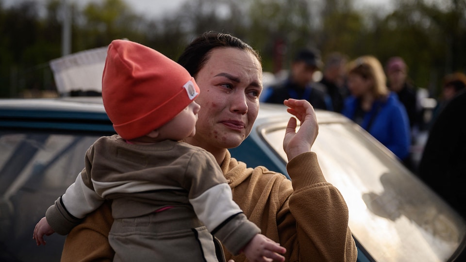 Une femme pleure alors qu'elle tient un jeune enfant dans ses bras après son arrivée d'un territoire occupé par la Russie dans une zone d'enregistrement et de traitement des personnes déplacées à Zaporijia, en Ukraine, le 2 mai 2022.