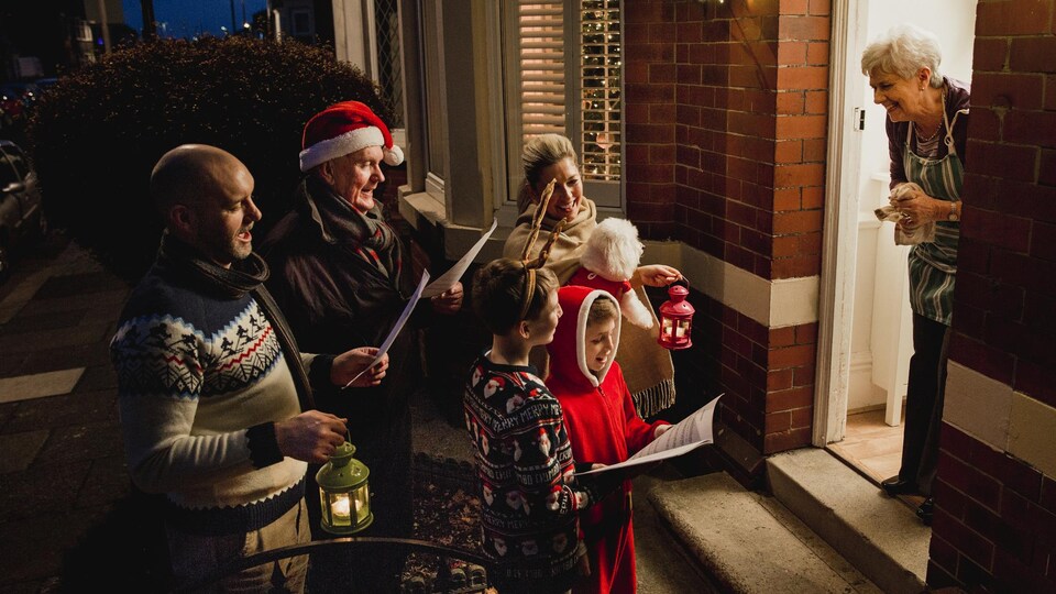 Trois générations d'une famille chantent à la porte d'une maison.