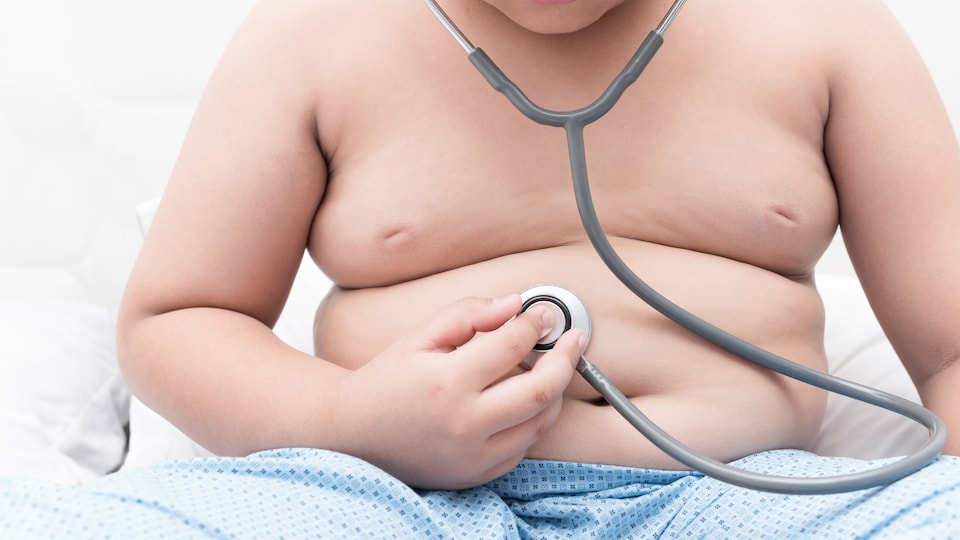 Un enfant obèse assis le torse nu porte un stéthoscope.