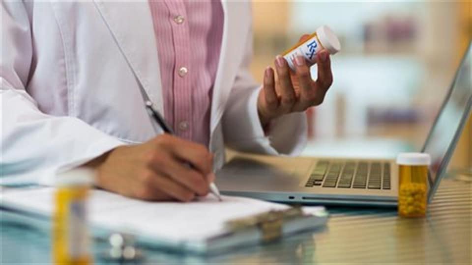 Un médecin prend des notes en tenant une bouteille de médicament. 