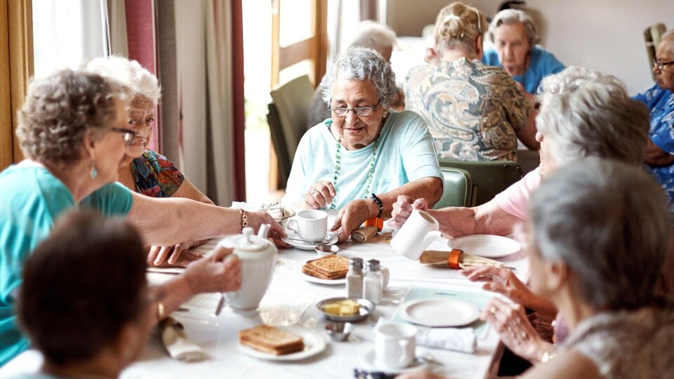 Plusieurs femmes âgées sont assises autour d'une table et prennent un café.