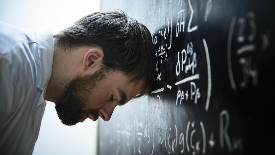 Un étudiant se frappe la tête contre un tableau où figurent de nombreuses équations scientifiques.