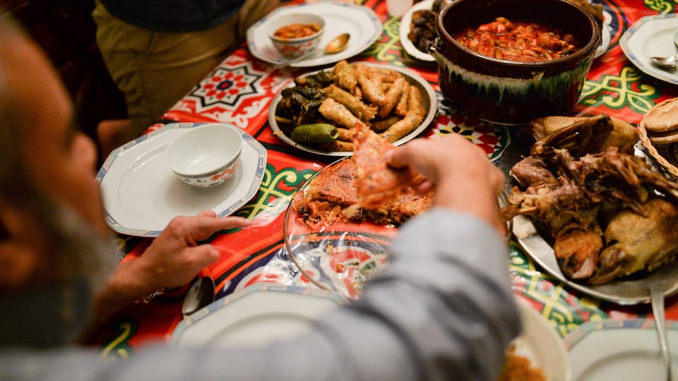 Une main d'homme se sert de la nourriture parmi plusieurs plats disposés sur une table colorée.