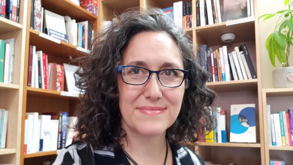 Happie Clara Testa pose devant des étalages de livres de sa librairie
