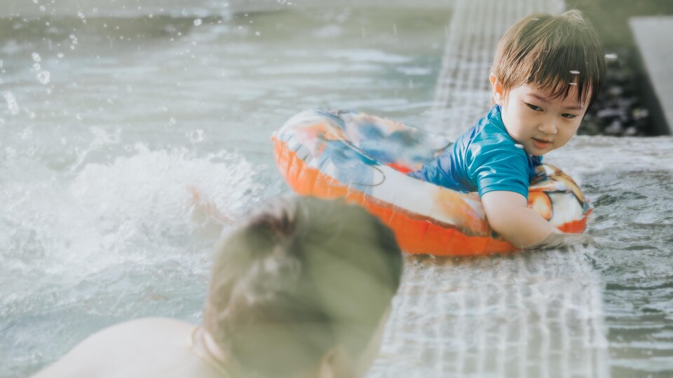 Un petit garçon est dans une bouée à la piscine, il regarde son papa. Les deux sont d'origine asiatique.