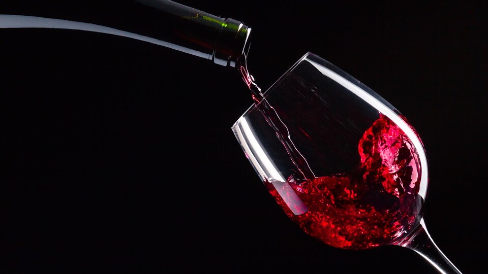Le contenu d'une bouteille de vin rouge est versé dans un verre.