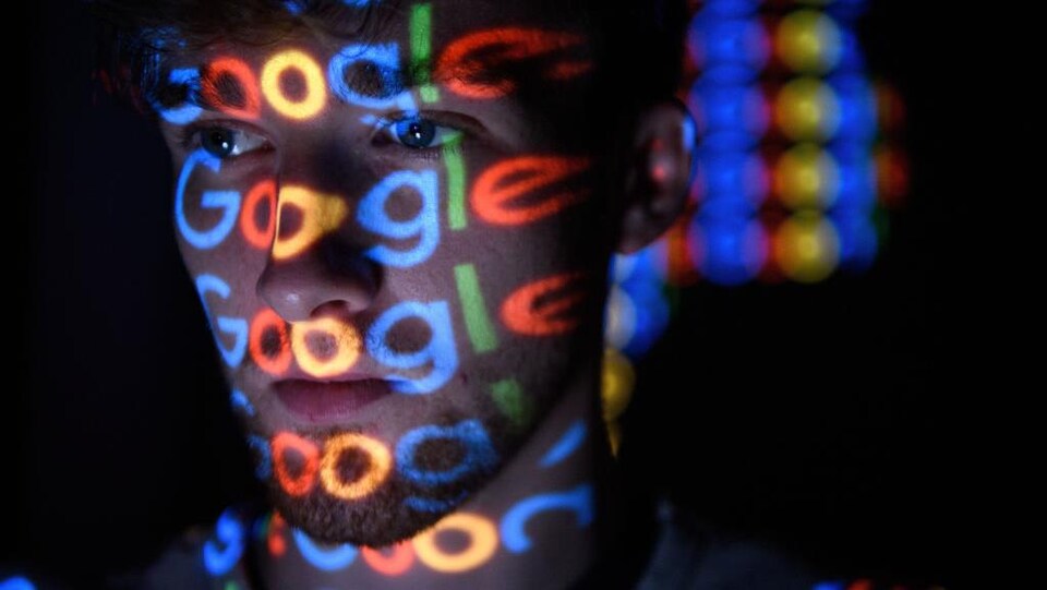 Le logo de Google luit sur le visage d'un homme dans la pénombre.