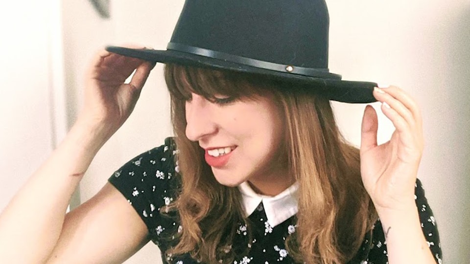 Une femme femme portant un chapeau, souriant et regardant le sol.