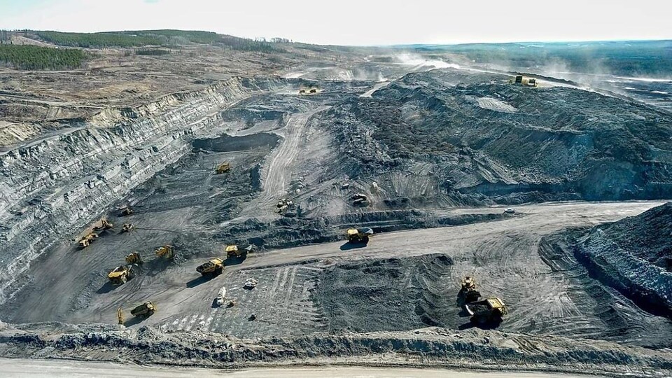 Une photo aérienne de la mine ou plusieurs camions à benne et tractopelles exploitent le minerai.