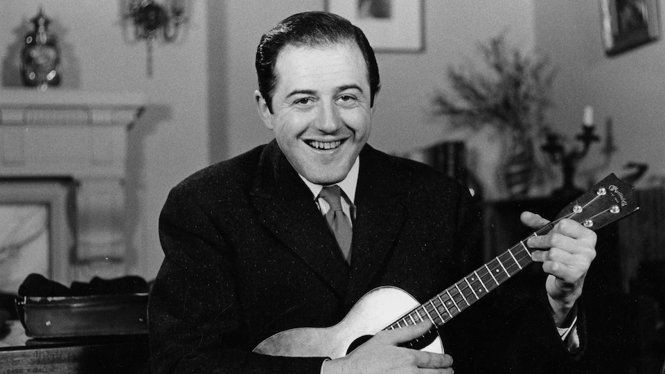 Le chanteur Raymond Lévesque tient une guitare dans le salon de sa résidence, en 1959.