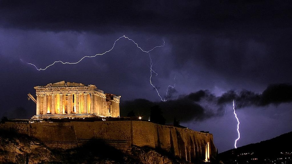 Photo de nuit du Parthénon illuminé, avec de la foudre en arrière-plan.