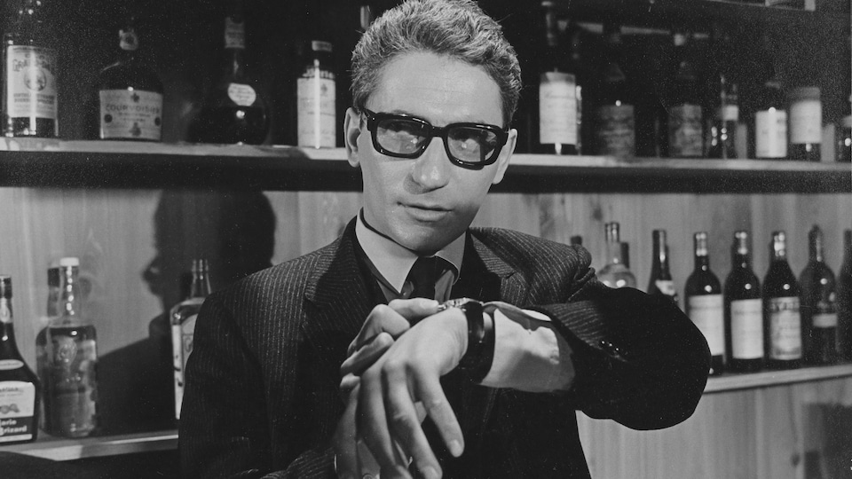 Hubert Aquin ajuste sa montre devant les étagères d'un bar dans une scène du film Faux bond (1966), de Louis-Georges Carrier.