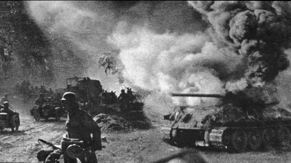 Photo en noir et blanc de soldats qui marchent près d'un tank en feu.