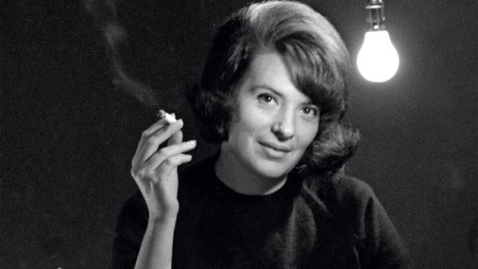 Marie Cardinal, devant une machine à écrire, sourit en tenant une cigarette.