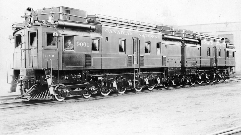 Photo en noir et blanc d'une locomotive de train du Canadian National avec un homme dans la cabine avant.