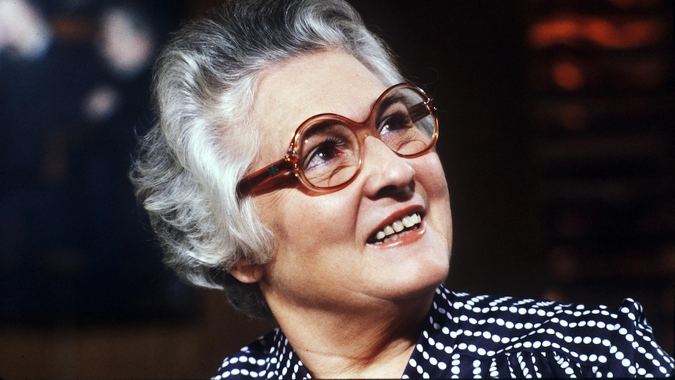 Une femme avec des lunettes sourit en regardant de côté légèrement vers les airs.