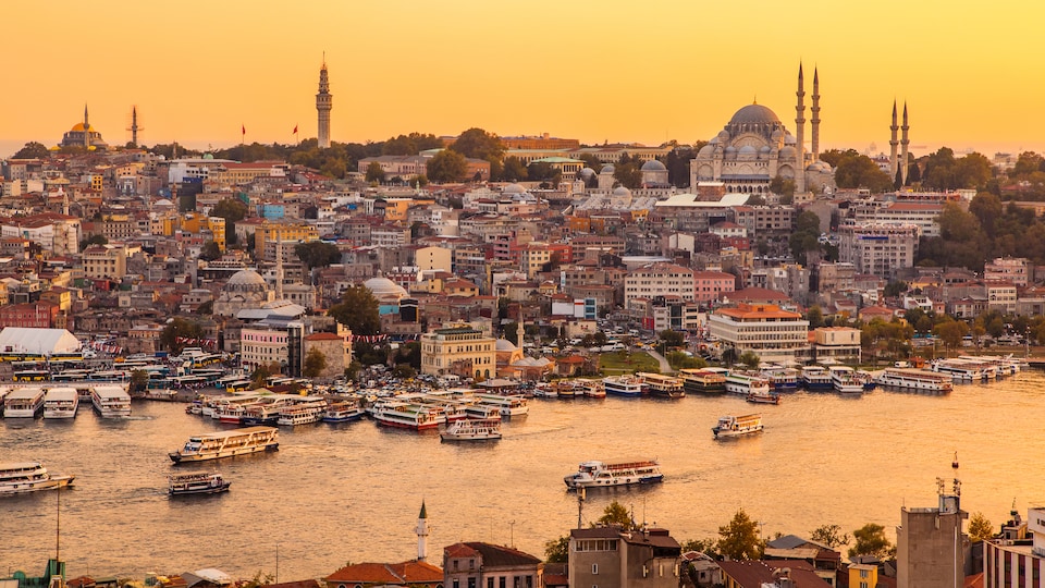 Vue d'Istanbul et de l'estuaire de la Corne d'Or au moment d'un coucher de soleil. Des bateaux traversent le cours d'eau et on peut voir l'église Sainte-Sophie.