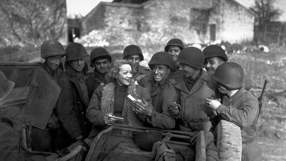 Photo en noir et blanc d'une femme entourée de soldats et qui donne une feuille de papier à l'un d'entre eux.