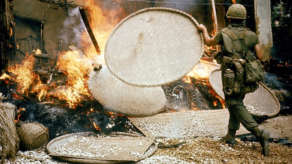 Un soldat lance un panier en osier dans une maison en flamme pendant la guerre du Vietnam.