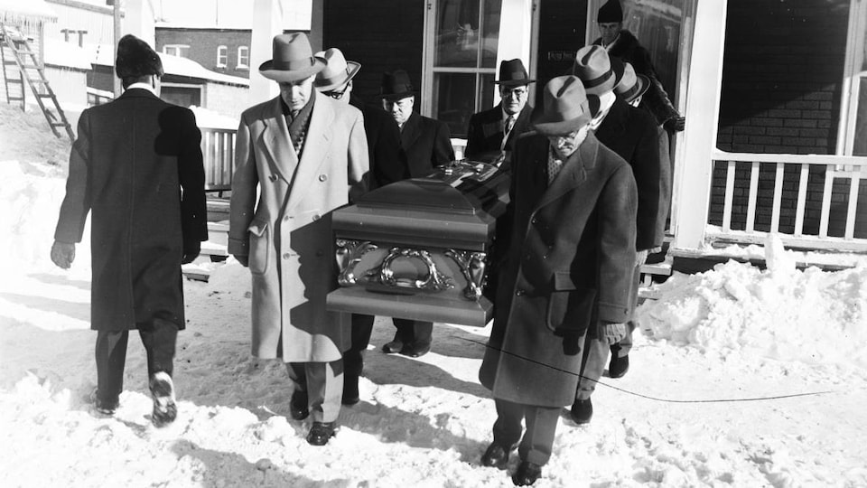 En hiver, des hommes sortent d'une maison en portant un cercueil.