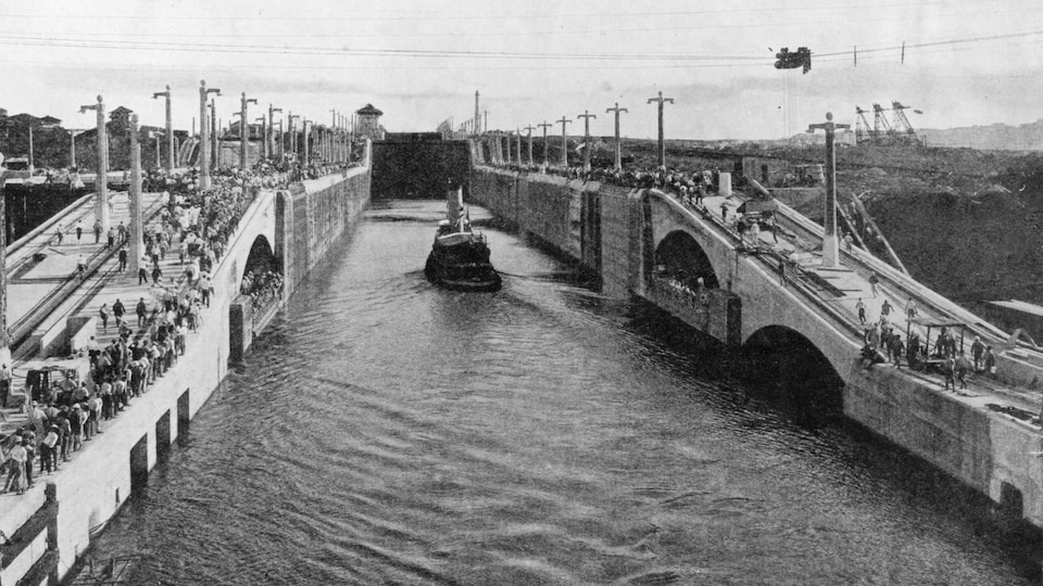 Photo en noir et blanc montrant un bateau à vapeur dans un canal étroit.