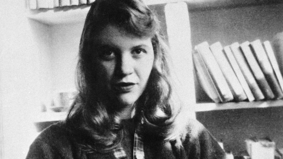 L'auteure Sylvia Plath, assise devant une bibliothèque.