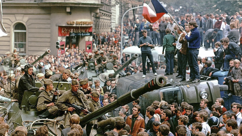 Des Praguois entourent un char d'assaut lors de l'invasion soviétique de la Tchécoslovaquie, en août 1968. Sur un camion renversé, un jeune tient un drapeau tchèque.