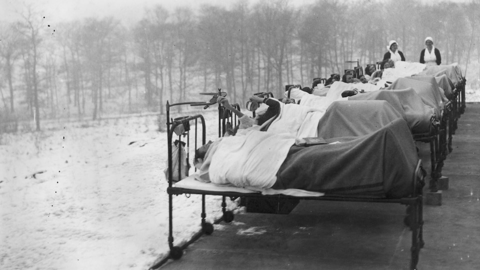 Photo en noir et blanc montrant des patients dans des lits d'hôpital à l'extérieur par une température hivernale.