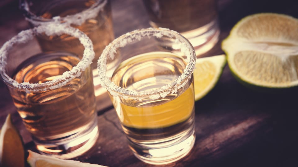 Des verres de tequila bordés de sel et des quartiers de lime sont déposés sur une table.
