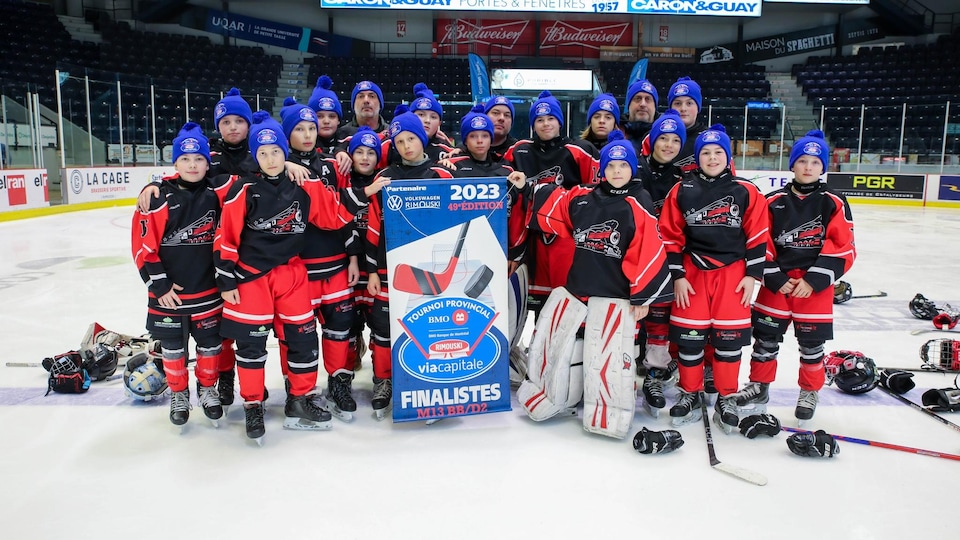 Une équipe de jeunes hockeyeurs sur la glace avec une affiche de tournoi.